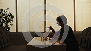 Silhouette of adult male sitting at the bistro bar, man having dinner alone, reading menu choosing meals.