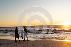 Silhouette african american boy with mother and father walking on beach against sky at sunset