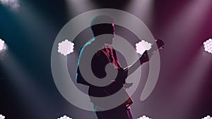 Silhouette of African American man in national ethnic dress plays electric guitar and dances to beat of music. Black