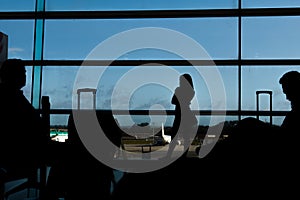 Silhouette of airline passengers in an airport lounge at the wide observation window watching an airplane flying of