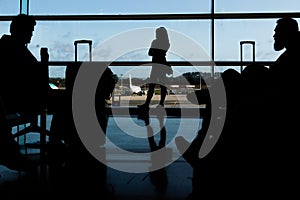 Silhouette of airline passengers in an airport lounge at the wide observation window watching an airplane flying of