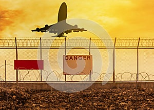 Silhouette airplane flying take off from runway with security razor barbed wire metal fence background