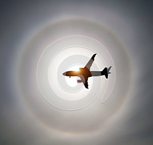 Silhouette of an airplane in the sky sun and halo in the clouds.