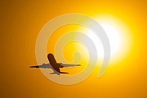 Silhouette of airplane taking off during sunset, flies near the disc of the sun.