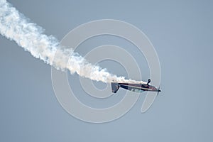 Silhouette of an airplane with trail of smoke behind against background of blue sky.