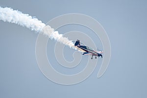 Silhouette of an airplane with trail of smoke behind against background of blue sky.