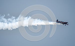 Silhouette of an airplane with trail of smoke behind against background of blue sky.