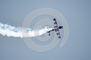 Silhouette of an airplane with trail of smoke behind against background of blue sky.