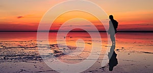 Silhouette of alone man looking toward vibrant sunset reflected in shallow waters of solt lake