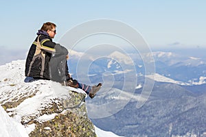 Silhouette of alone tourist sitting on snowy mountain top enjoying view and achievement on bright sunny winter day. Adventure,