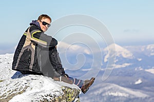 Silhouette of alone tourist sitting on snowy mountain top enjoying view and achievement on bright sunny winter day. Adventure,
