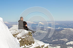 Silhouette of alone tourist sitting on snowy mountain top enjoying view and achievement on bright sunny winter day. Adventure,