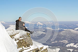 Silhouette of alone tourist sitting on snowy mountain top enjoying view and achievement on bright sunny winter day. Adventure,