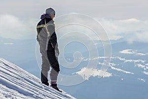 Silhouette of alone tourist standing on snowy mountain top enjoying view and achievement on bright sunny winter day. Adventure,