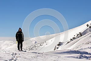 Silhouette of alone tourist standing on snowy mountain top enjoying view and achievement on bright sunny winter day. Adventure,