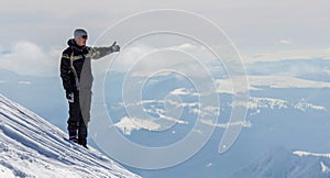 Silhouette of alone tourist standing on snowy mountain top in winner pose with raised hands enjoying view and achievement on