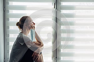 Silhouette of alone woman sitting on the windowsill on the background of window. Quarantine, self-isolation, stay at home. Concept