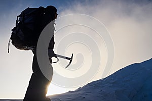Silhouette of alpinist man going to the top of mountain at sunrise. Holding an ice tool in his hands