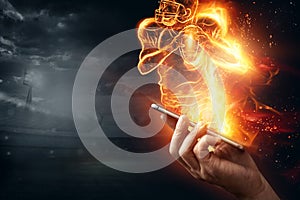 A silhouette of an American football player on fire crawls out of a smartphone. Online sports concept, speed, bet, american game photo
