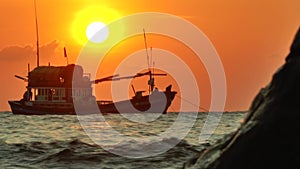 Silhouette of the anchored fishing boat in the rays of the setting sun swinging in the waves