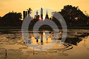 Silhouette of ancient Buddha statue and pagodas against sunset sky at Sukhothai, Thailand.