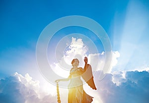 Silhouette of angel statue sculpture with sunlight shining behind white cloud with blue sky background.