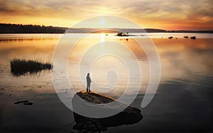 Silhouette of angler on sunset. Sun reflecting in water with stones and islands. Baltic sea, gulf of Finland