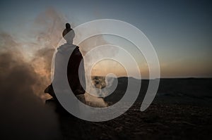 Silhouette of Arab man stands alone in the desert and watching the sunset with clouds of fog. Eastern Fairytale