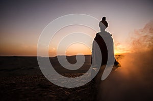 Silhouette of Arab man stands alone in the desert and watching the sunset with clouds of fog. Eastern Fairytale