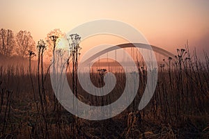 Silhouette of an arch bridge above the river covered with thick fog during sunset