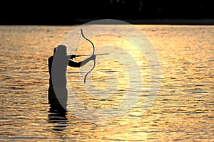 Silhouette archery shoots a bow at a target in sunset sky