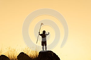 Silhouette of Asian Boy scouts stand on rocky mountains holding flags in their hands to show success on mountain top over sky and