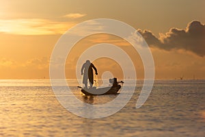Silhouette of asian Fisherman on a traditional wooden boat during sunrise