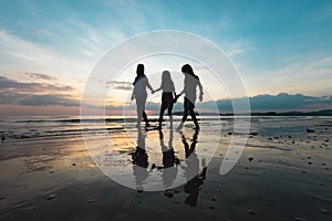 Silhouette of asian mother and two daughters holding hand and walking on the beach together at the sunset time