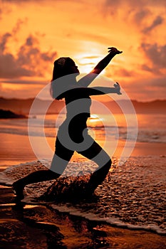 the silhouette of an asian teenager in black clothes posing with her body above the seaside waves very beautifully