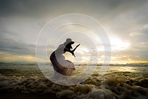 Silhouette of asian woman playing water in the sea with wave on the beach and enjoying beautiful nature in the sunset time.