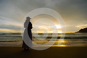 Silhouette of asian woman wearing stylish hat and clothes looking to the ocean and enjoying beautiful Sunset on the Beach.