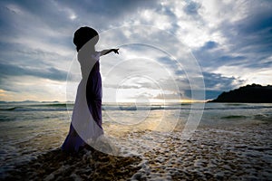 Silhouette of asian woman wearing stylish hat and clothes pointing at the sky and looking to the ocean