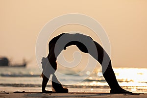 Silhouette of Asian young woman practice Yoga bridge Pose on the sand and beach