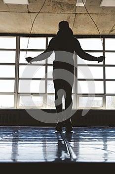 Silhouette Athlete man jumping rope in the gym in front of large panoramic windows