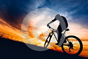 Silhouette of athlete riding mountain bike on hills at sunset