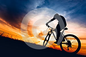 Silhouette of athlete riding mountain bike on hills at sunset photo