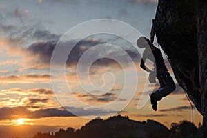 Silhouette of athletic woman climbing steep rock wall