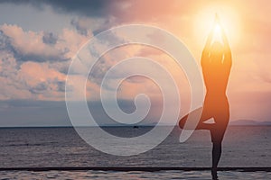 silhouette Athletic woman practice yoga lotus pose to meditation summer vacation on pier with sunset sea beach