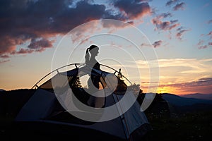 Silhouette of an attractive girl standing in profile near the tent under the evening sky at daybreak