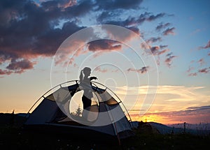 Silhouette of an attractive girl standing in profile near the tent under the morning sky at daybreak