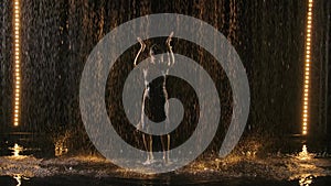 Silhouette of an attractive woman in a wet tight dress enjoying a flamenco dance in the rain. Black background with