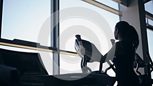 Silhouette of attractive young woman at the gym exercising on the xtrainer machine