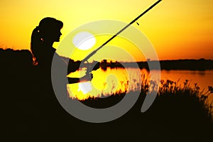 Silhouette of awoman with a fishing rod on the river bank