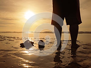 Silhouette back view of young man standing at golden sunset beach with his sandals